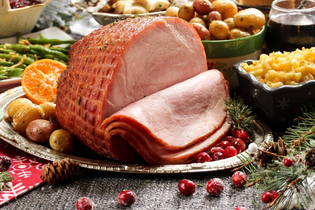 A cut-up piece of ham surrounded by side dishes, including mac and cheese and potatoes.