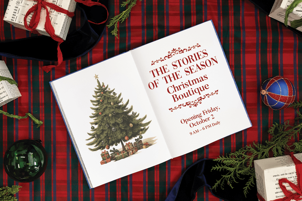 An open-face book with a Christmas tree on the left page and "The Stories of the Season Christmas Boutique, opening Friday, October 2 from 9AM to 6PM daily" on the right page.