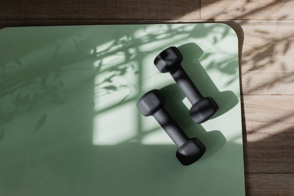 Yoga mat and dumbbells on floor with shadow sunlight.