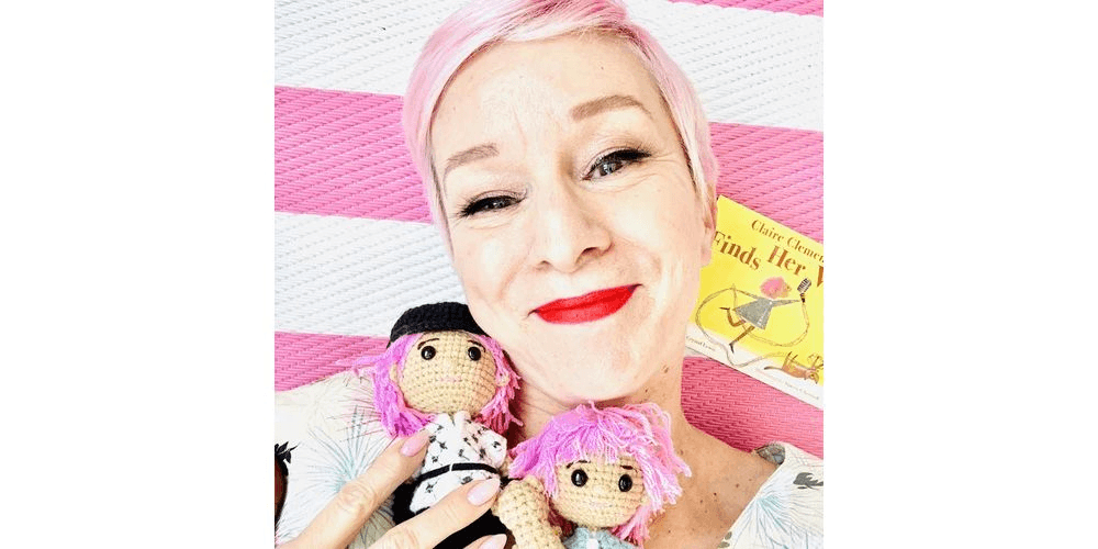 Woman with oink hair holding two dolls with pink hair